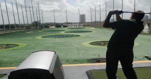 Man swinging a golf club with the golf course in front of him. | San Antonio, TX