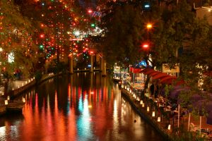Riverwalk in San Antonio at night well lit with colorful lights in the trees on both sides of the river. | San Antonio, TX
