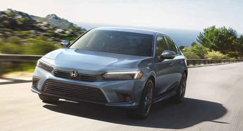 Honda Civic trim comparison A 2023 Honda Civic Sport in the color Sonic Gray Pearl racing down the road in a lush, mountain area